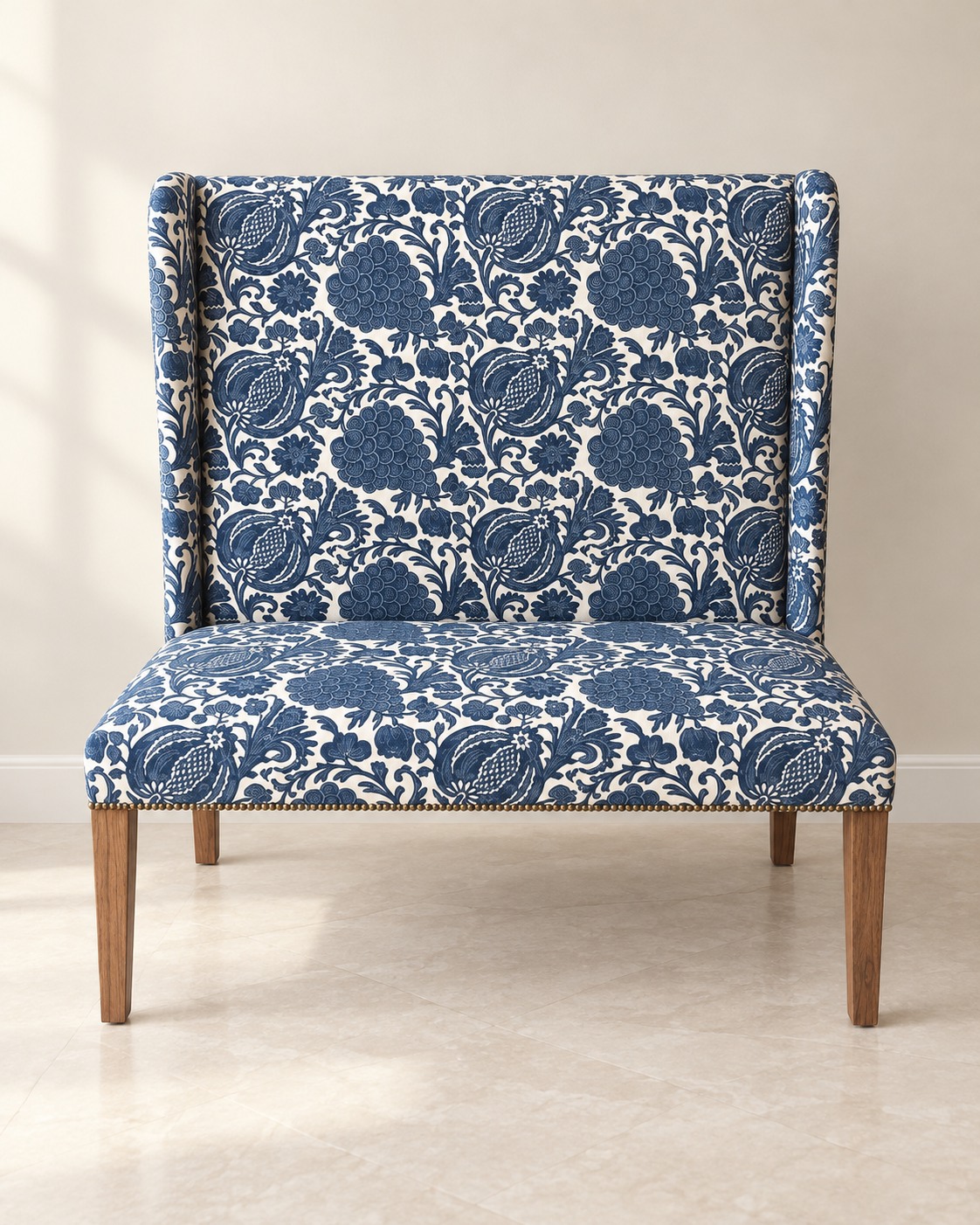Intricate blue botanical motifs cover an ivory ground across a tall-backed settee. Slim wood-toned legs and a row of small studs add a restrained finishing detail.
