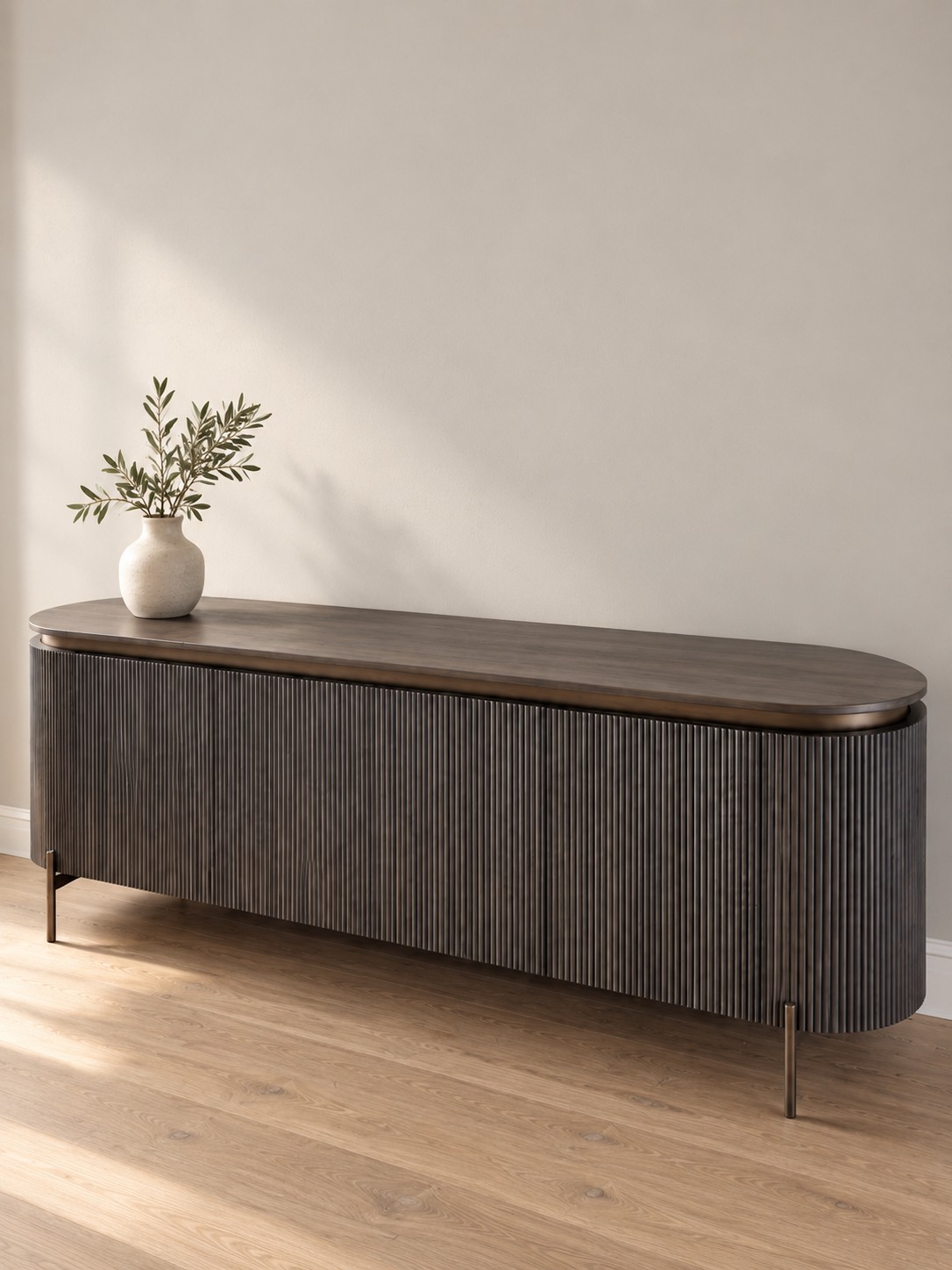 Fine vertical fluting wraps around a long, rounded silhouette. A deep wood tone and slender legs give this storage piece a quiet, architectural presence.