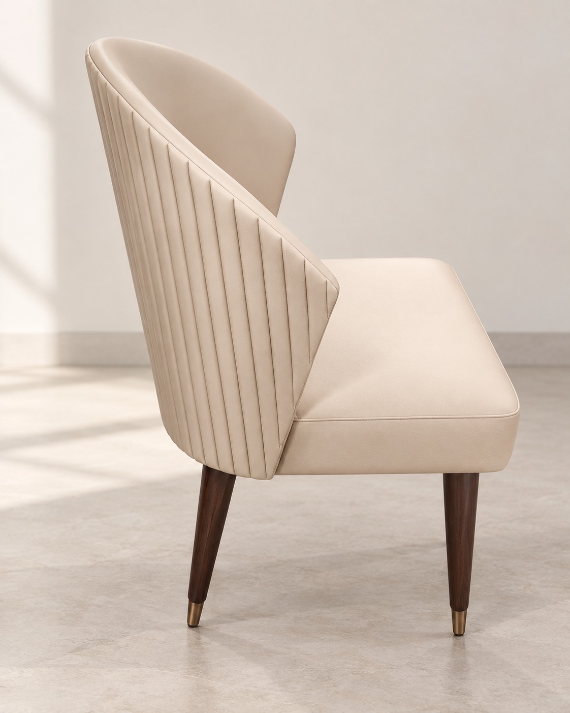 Vertical channels follow the curved ivory back, bringing texture to a clean silhouette. Dark tapered legs with gold-toned tips add a subtle contrast.