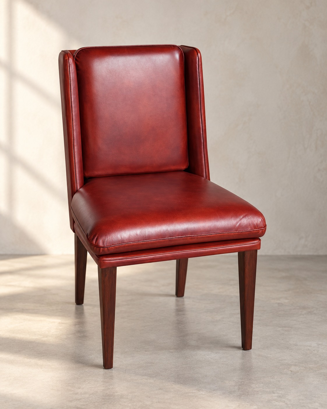 Rich oxblood upholstery wraps a tall, gently winged back and cushioned seat. Dark tapered legs keep the profile clean and composed.