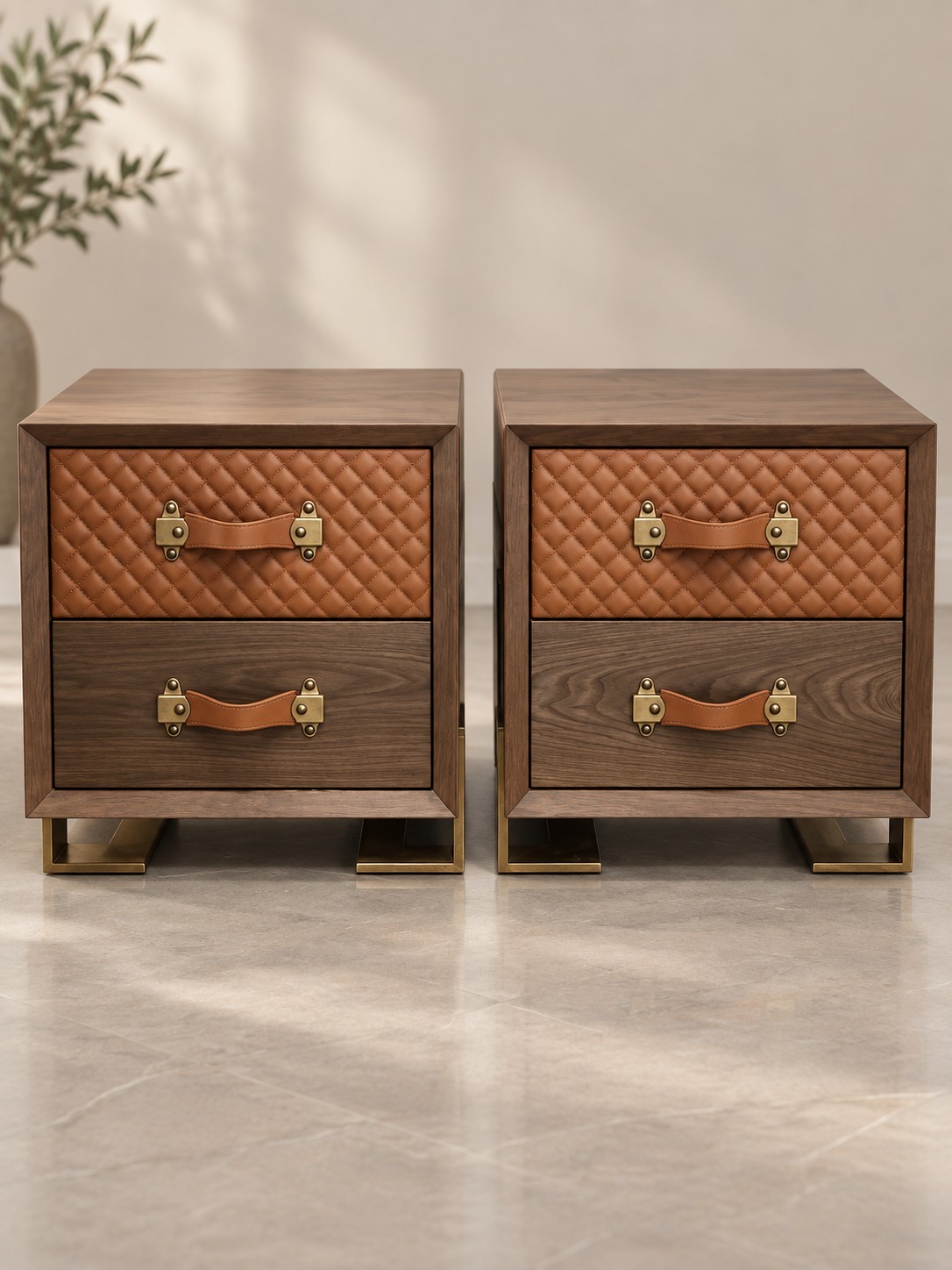 Warm wood grain frames tan quilted drawer fronts and strap-style handles. Gold-toned fittings and open rectangular feet give these bedside tables a distinctive finishing touch.
