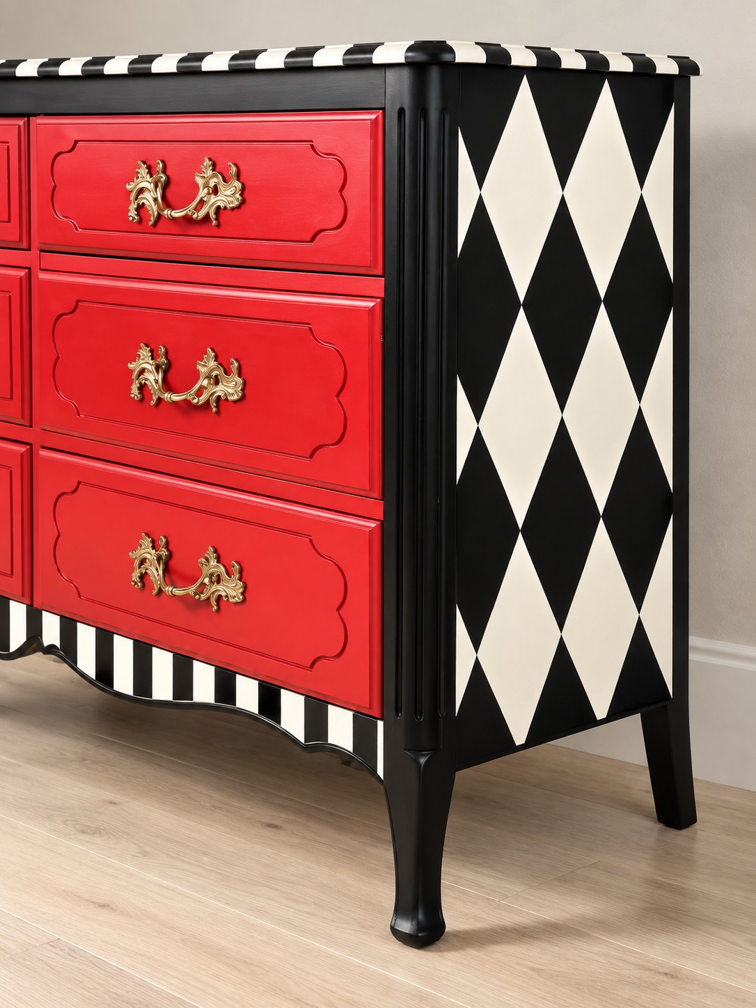 Vivid red drawer fronts pair with black and ivory diamond panels and striped trim. Ornate gold-toned handles bring a playful flourish to this expressive chest.