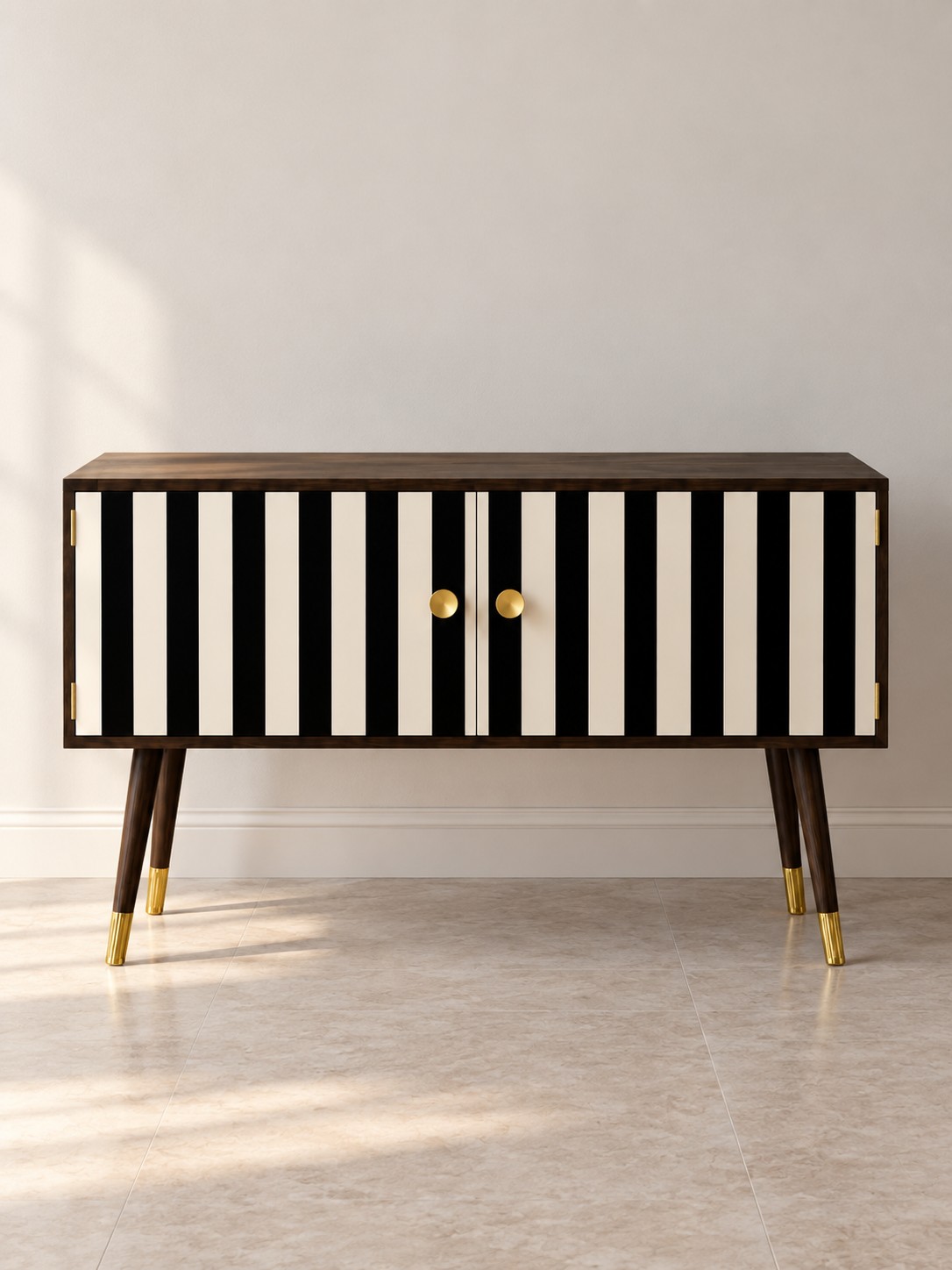 Black and ivory striped doors sit within a dark wood frame. Gold-toned knobs and tipped legs add a bright finishing detail to this statement cabinet.