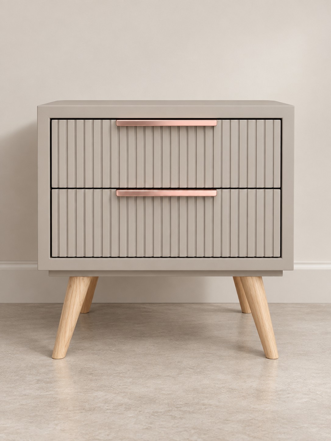 Fine vertical grooves bring texture to two taupe drawer fronts. Blush-toned handles and splayed pale wood legs add warmth to the clean, compact form.