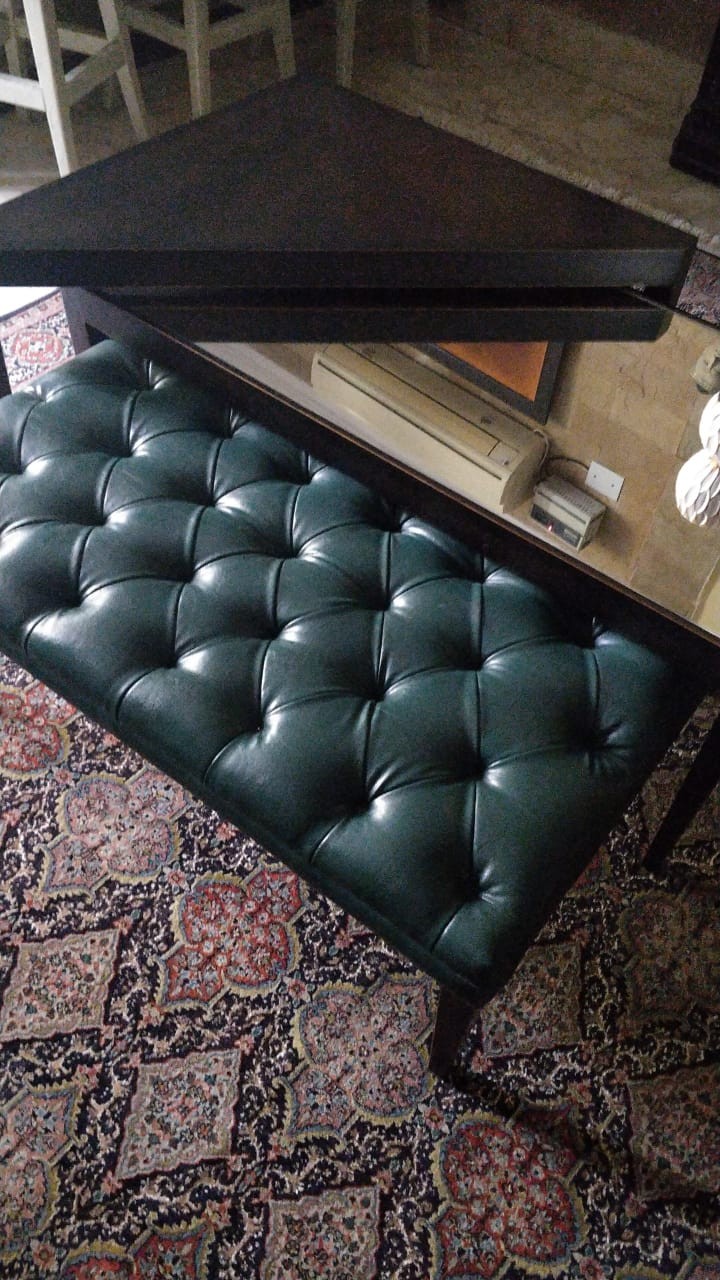 Deep green tufted bench beside a reflective table on a multicoloured patterned rug.